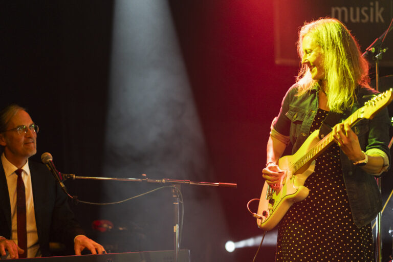 Sarah, Gitarristin der Beatroller, konzentriert beim Liveauftritt, Keyboarder Norbi im Hintergrund